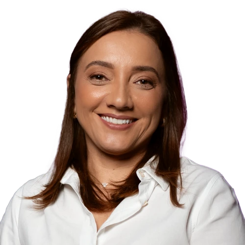 Professora Vanessa Soares, uma mulher de pele clara com cabelos e olhos castanhos, sorrindo e vestindo uma camisa social branca, em um fundo escuro.